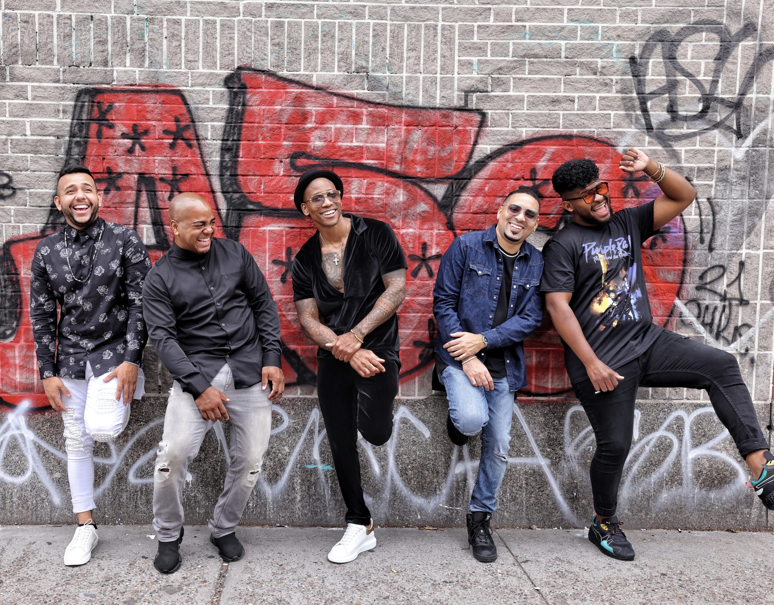 Pedrito Martinez and his band laughing in front of graffiti.