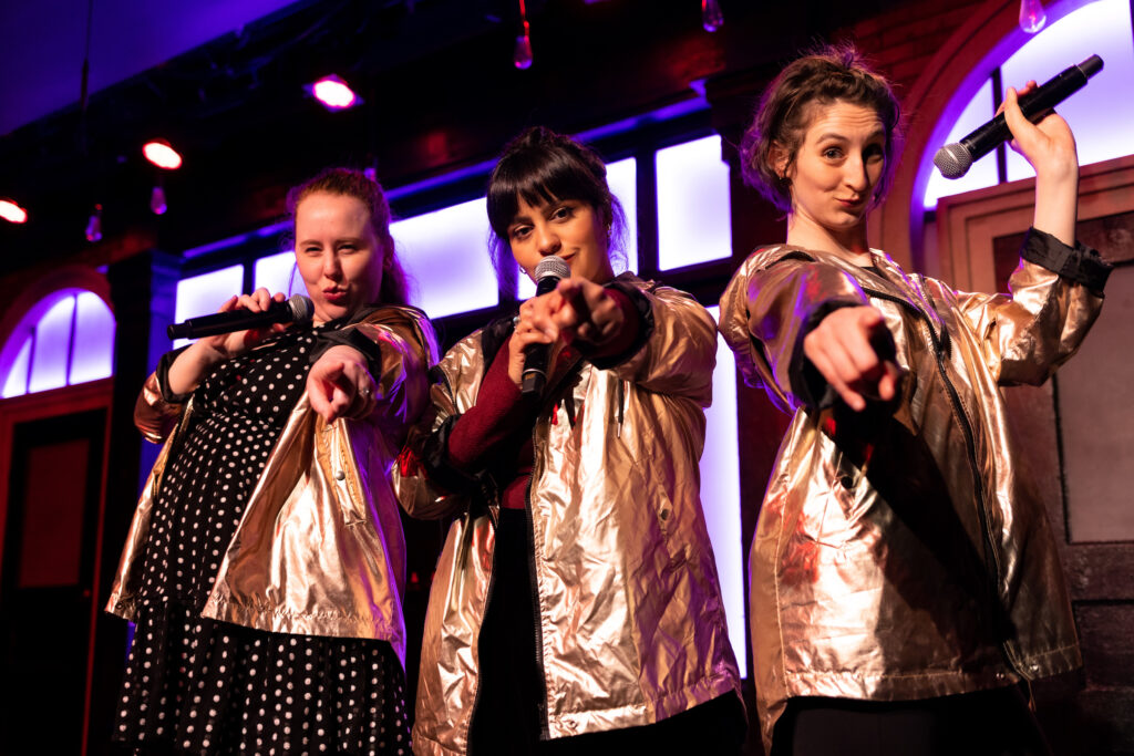 Members of The Second City Touring company performing in gold jackets.