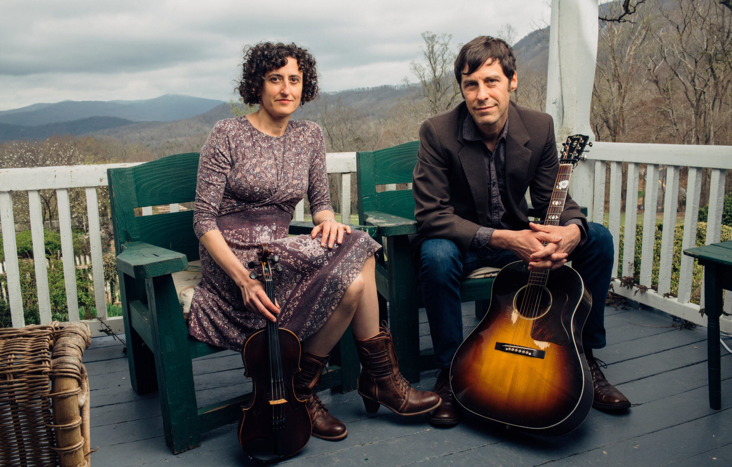 Zoe and Cloyd sit on a porch with their instruments, the mountains in the distance. Photo by Sandlin Gaither.