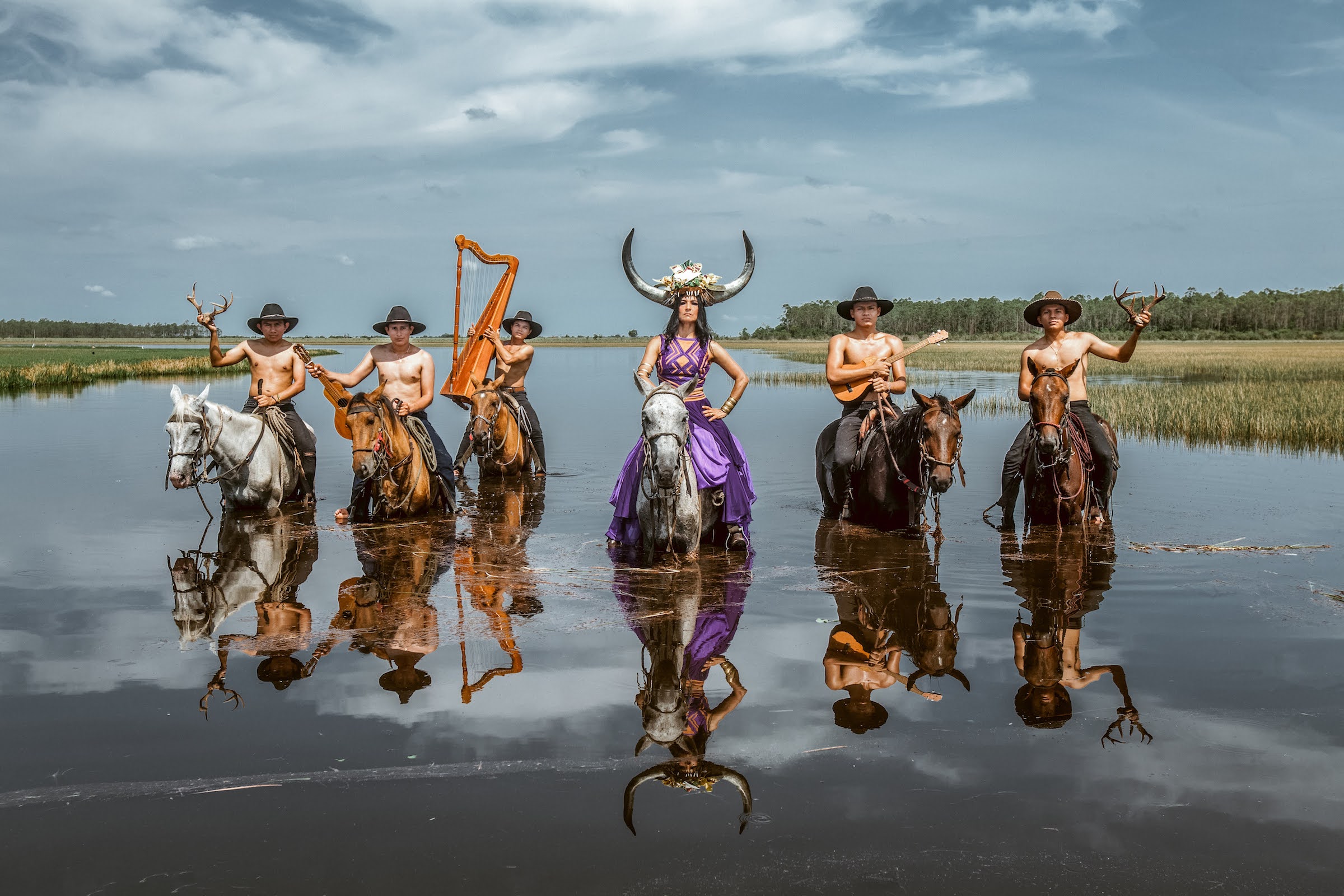 Band members from Cimarron in a river on horseback holding antlers and instruments.