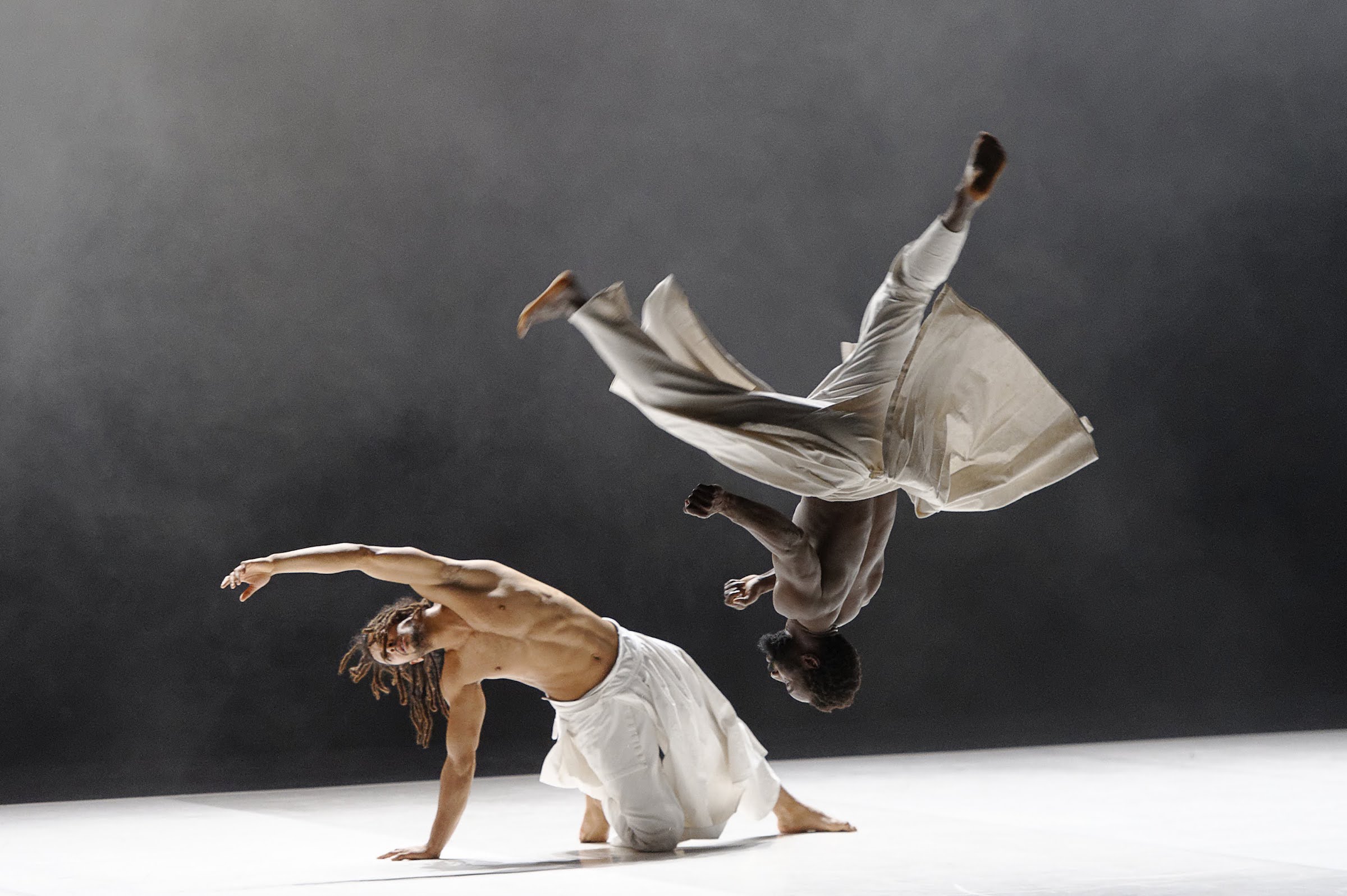 Two dancers from Company Herve Koubi - one caught flipping in midair, one with on a knee with one arm outstretched. Photo by Nathalie Sternalski.