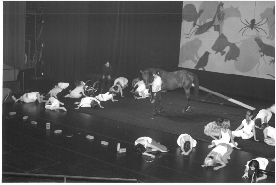  a circle of children lay on the floor while a woman leads a horse around the stage