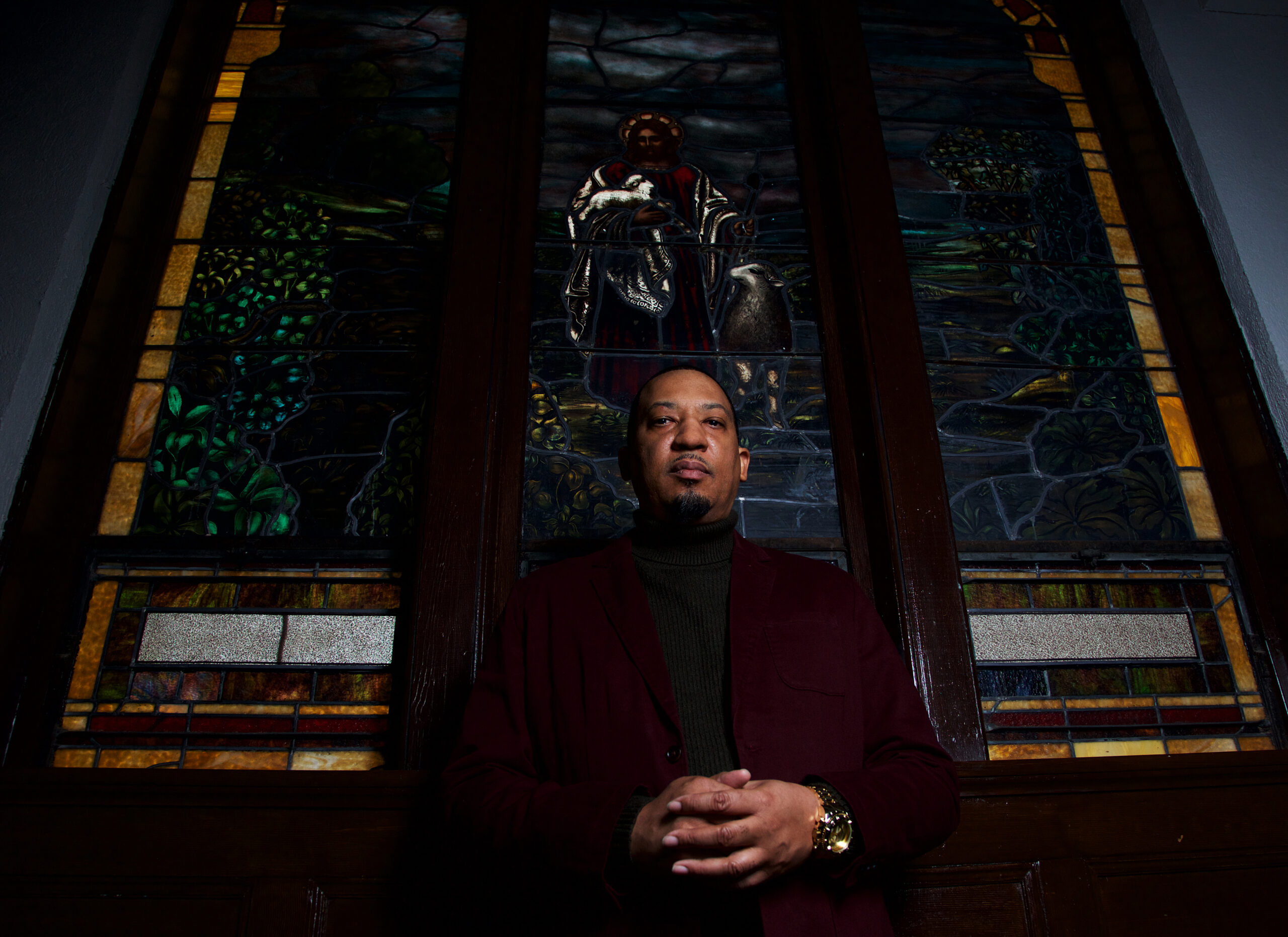 Dasan Ahanu clasps his hands in front of a stained glass window.