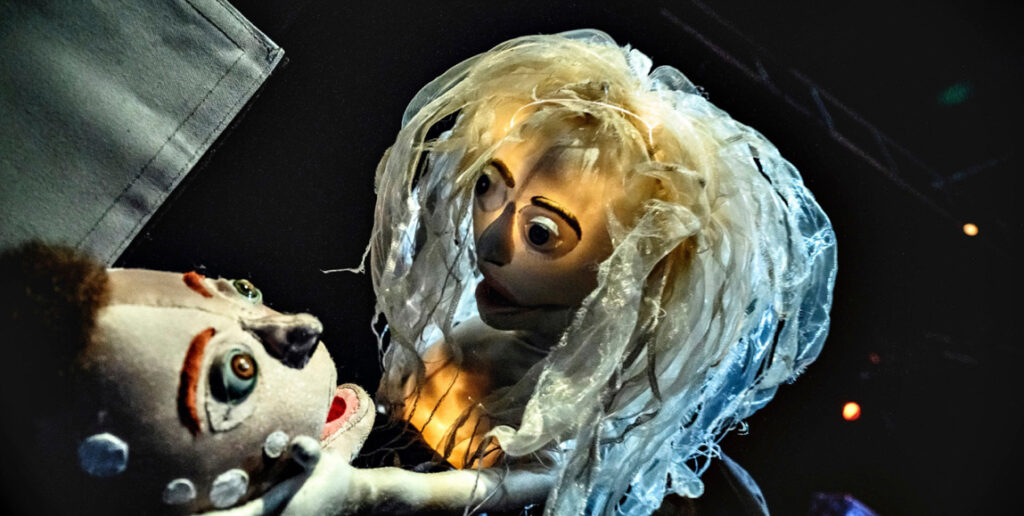 Two puppets hold each others faces while speaking.