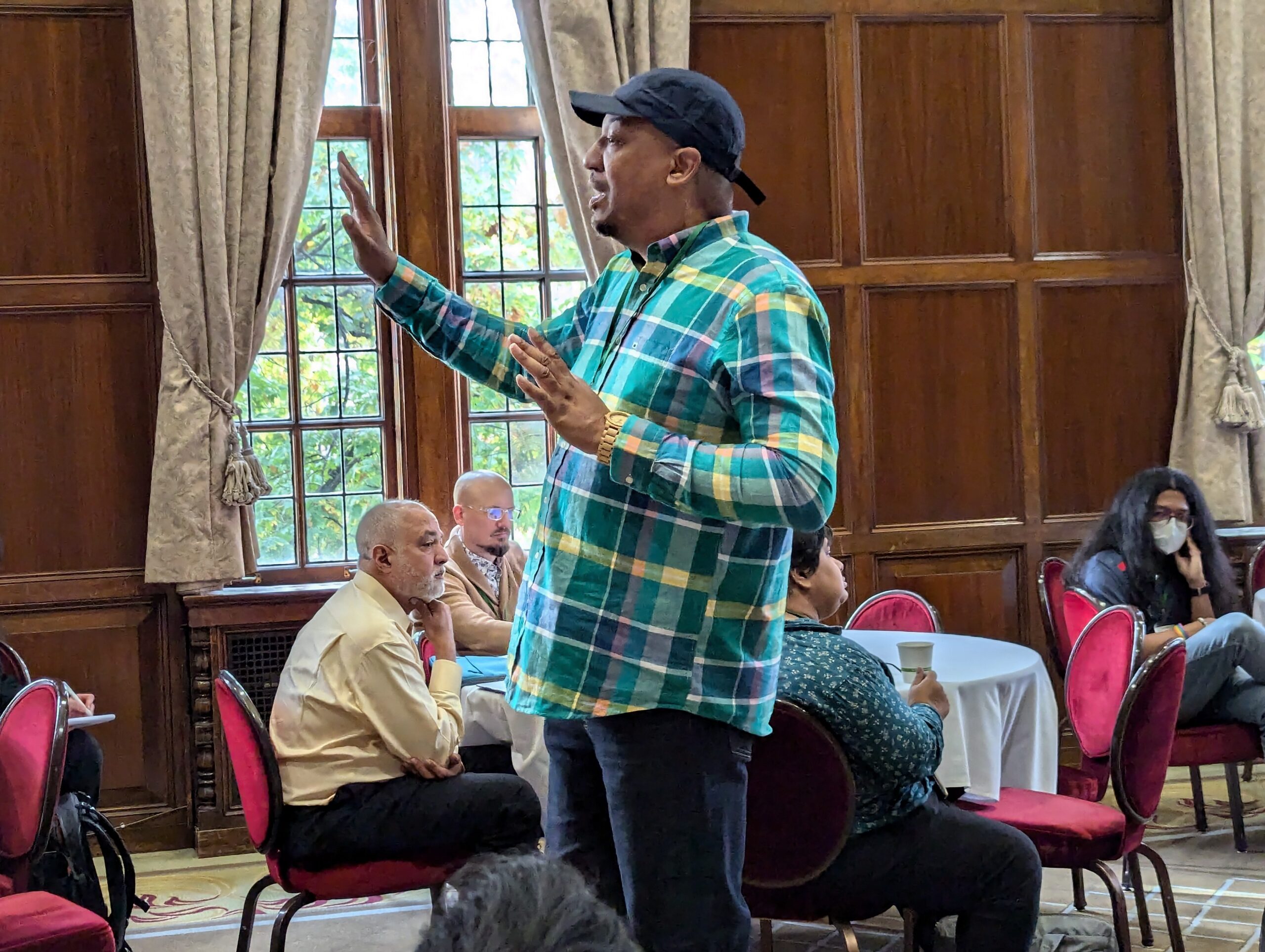 Dasan Ahanu stands with hand lifted, speaking to audience.