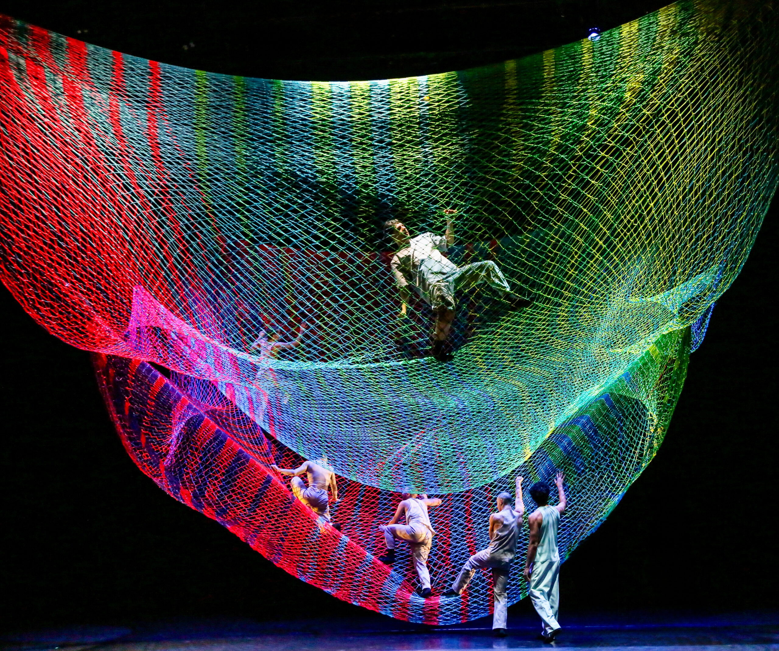 Dancers climb up to be suspended in a colorful net.
