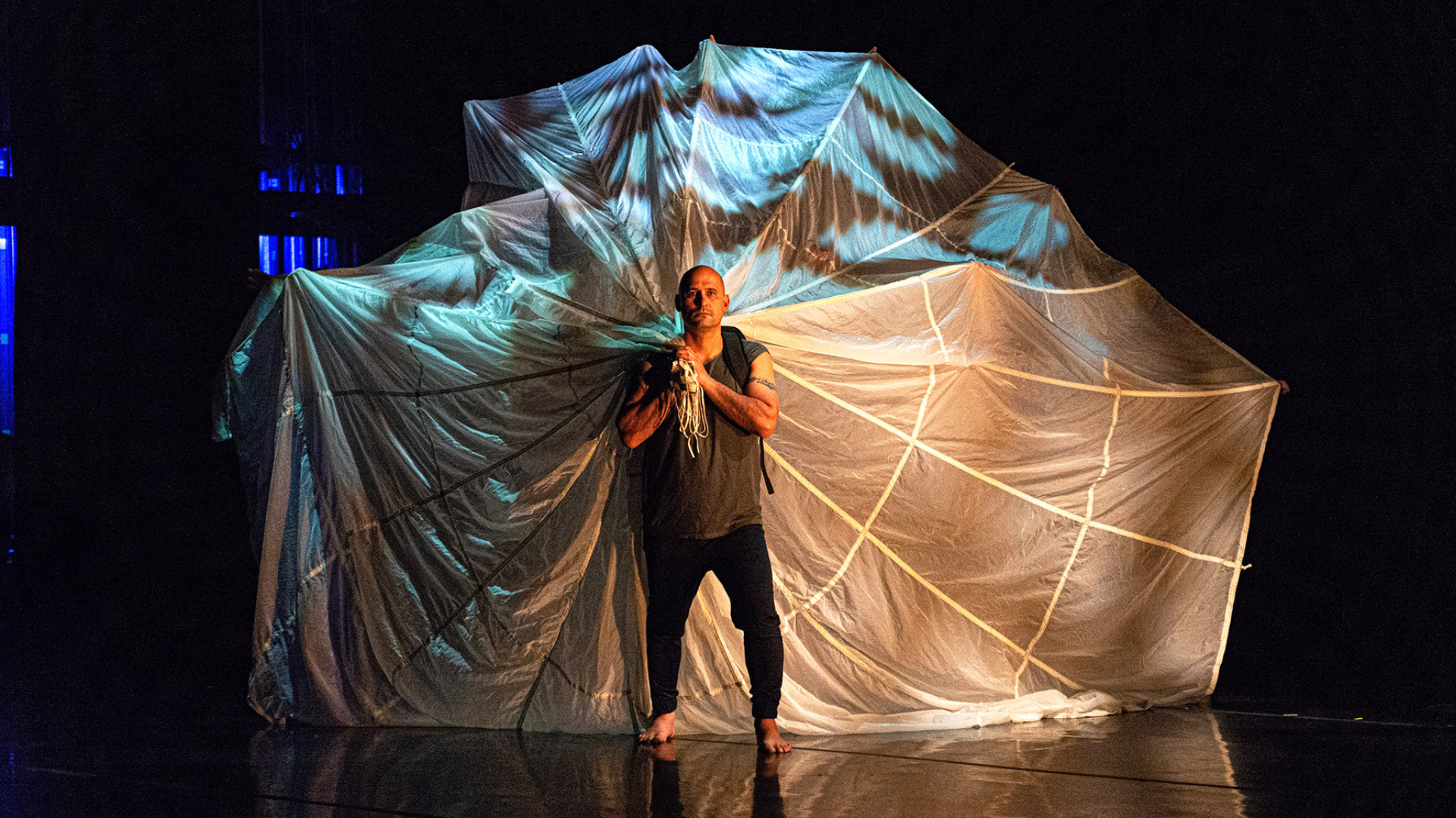 Founding company member Alfredo Hurdato on stage holding a parachute behind him. Photo courtesy of artist.
